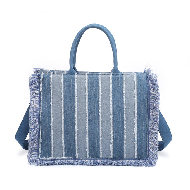 Back of a blue striped rectangular tote bag with fringed edges, rounded handles and a shoulder strap.