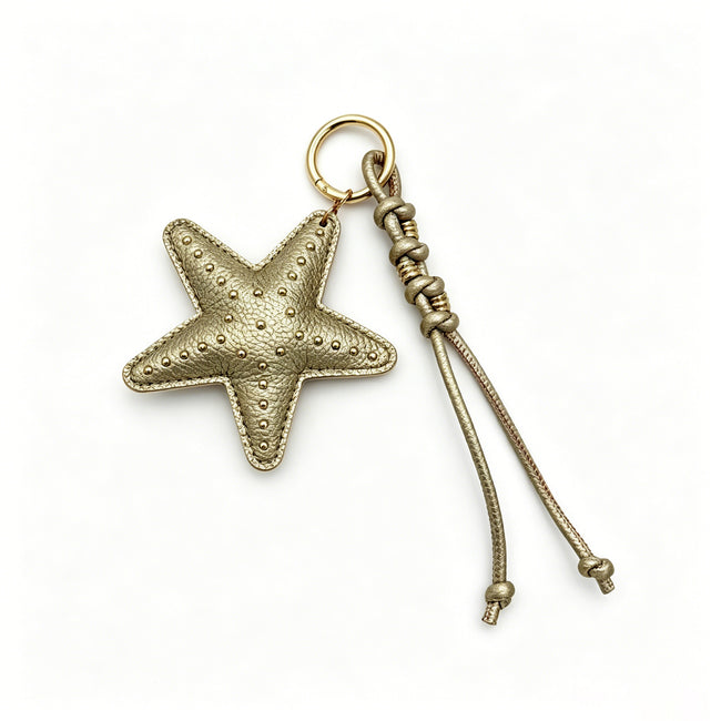 Gold-colored starfish keyring with small studs and knotted dangling cords.