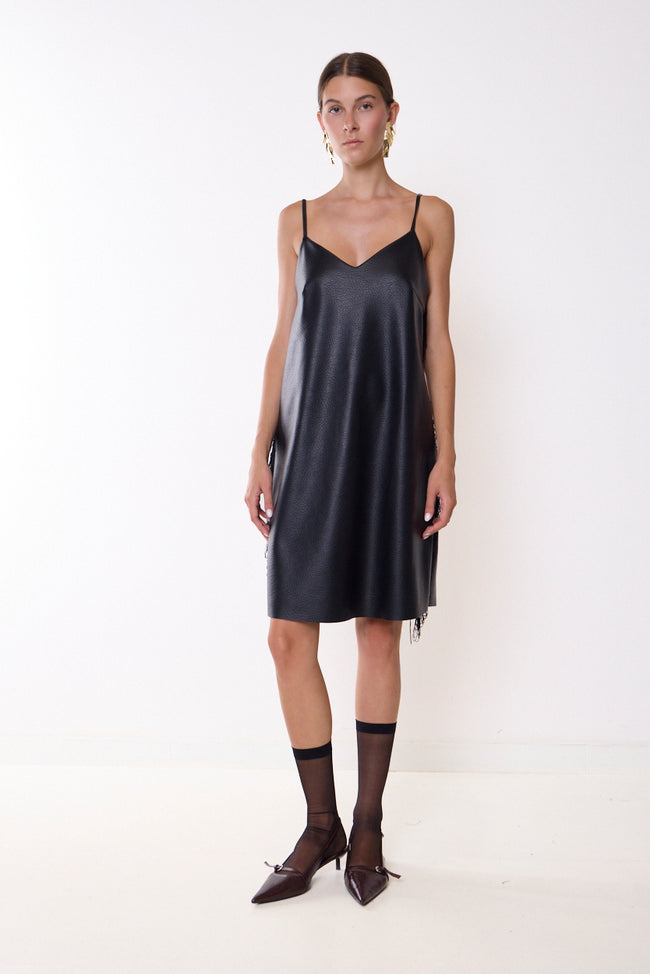 Black faux-leather slip dress with V neckline, narrow shoulder straps, side hanging fringe and back zip; socks, shoes and earrings styled separately