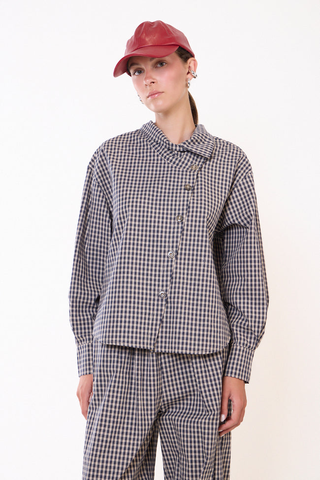 Black and white checks checked blouse with asymmetric folded collar, diagonal front buttons, long sleeves and buttoned cuffs; checked trousers or jeans, cap and shoes styled separately