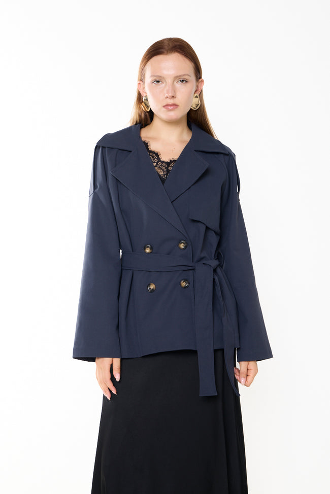 Dark navy blue cropped double-breasted trench jacket with notched lapels, shoulder tabs, front storm flap and waist tie; trousers and earrings styled separately