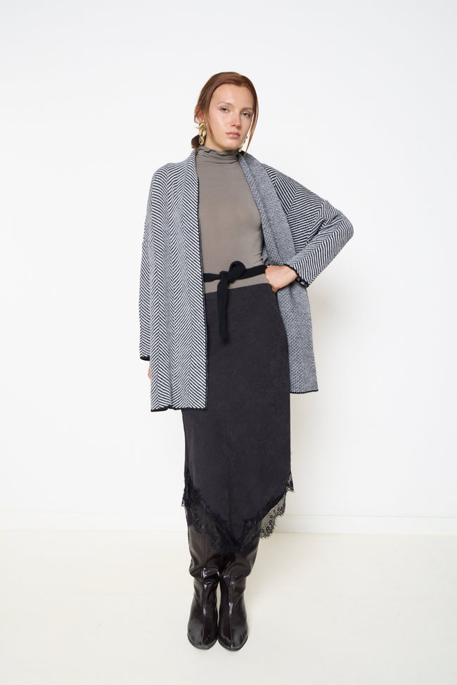 Black and cream chevron-knit open-front longline cardigan with long sleeves, contrasting cuff and hem edging and side hem slits; turtleneck top, belt, lace-trim skirt and boots styled separately