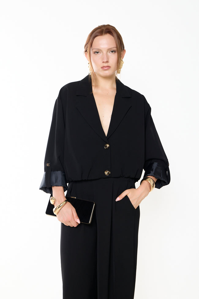 Black cropped boxy two-button blazer with notched lapels, turned contrast cuffs and cuff button-tab details; matching wide-leg trousers, bag and gold-tone accessories styled separately