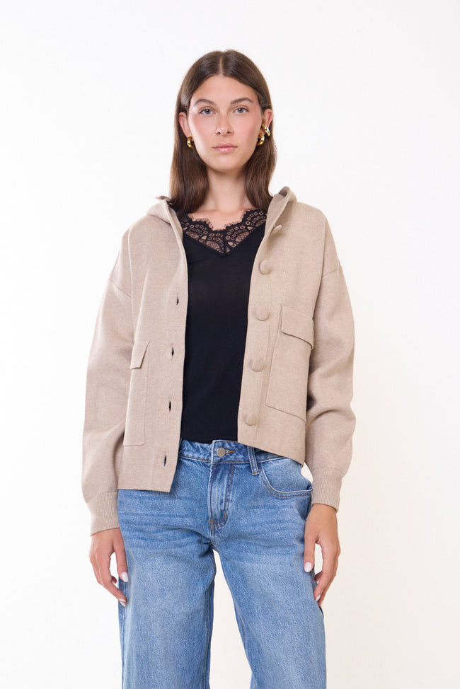 Beige cropped hooded button-front utility coat with long sleeves and two front flap patch pockets; lace-trim top and trousers styled separately