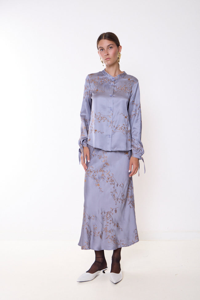 Grey lilac-toned long flared skirt with floral vine and scrolling embroidery; coordinating embroidered blouse and shoes styled separately