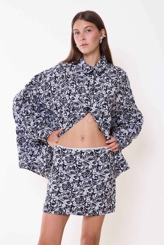 Black and cream rose-pattern jacquard mini skirt with contrast waist-edge trim and straight mini silhouette; coordinating shirt jacket, lace top and accessories styled separately