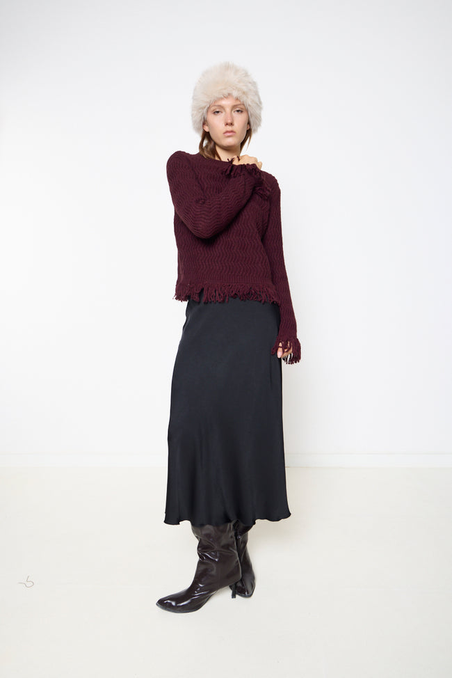 Bordeaux wine round-neck textured knit sweater with wavy knit pattern, long sleeves and fringe along hem and cuffs; midi skirt and hat styled separately