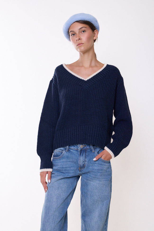 Dark navy blue textured V-neck knit sweater with contrast neckline and cuff trim, long sleeves and ribbed hem; jeans, cap and accessories styled separately