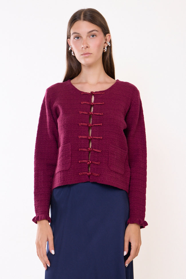 Bordeaux wine textured round-neck knit cardigan with front knotted loop fastenings, two patch pockets and ruffled cuff edges; skirt and earrings styled separately