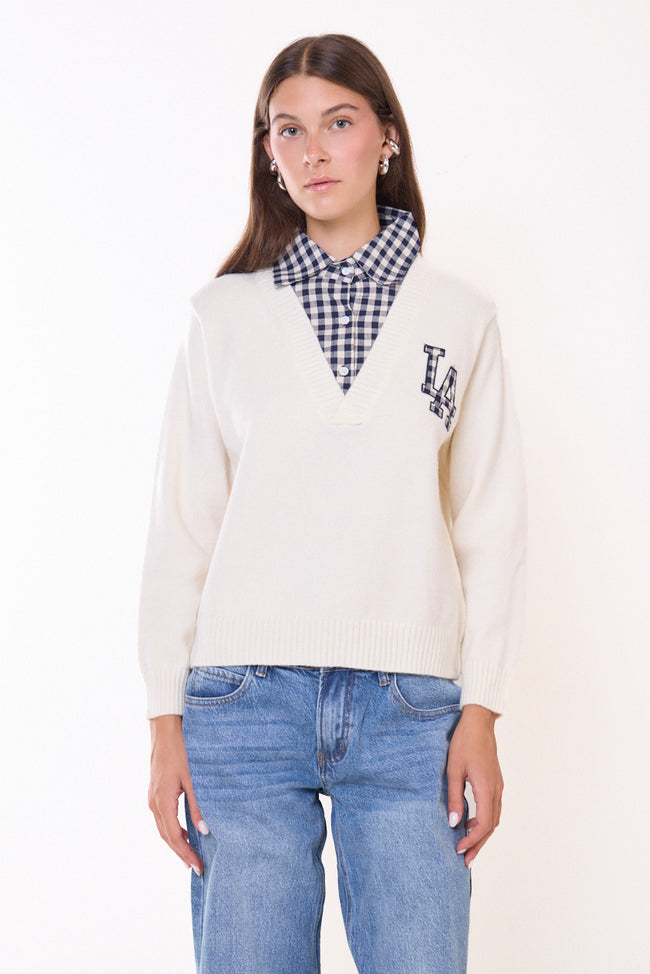 White cream V-neck knit sweater pictured with checked shirt-style collar and front detail, checked LA letter appliqué, long sleeves and ribbed cuffs and hem; jeans and jewellery styled separately