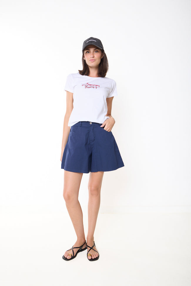 Dark blue cotton-elastane tailored shorts with flared A-line legs, button and zip fly, belt loops and side pockets; white T-shirt and cap styled separately