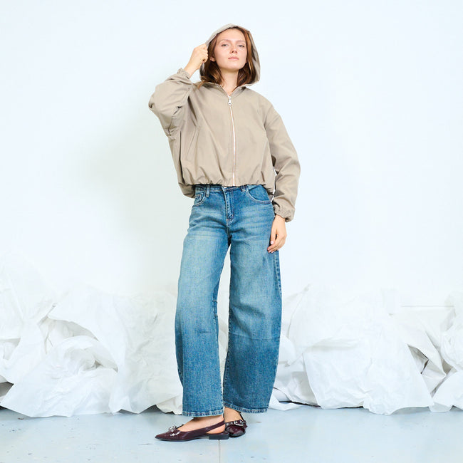 Beige cropped hooded zip-front jacket with long sleeves, side pocket openings and gathered cuffs and hem; plain top, jeans and shoes styled separately