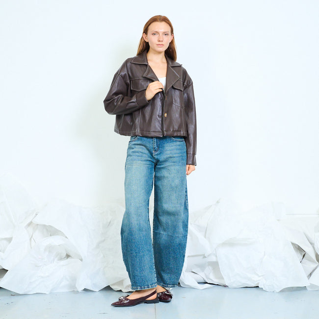 Coffee brown cropped faux-leather jacket with notched lapels, front buttons, contrast chest flap details, long sleeves and panel topstitching; plain top, jeans and shoes styled separately