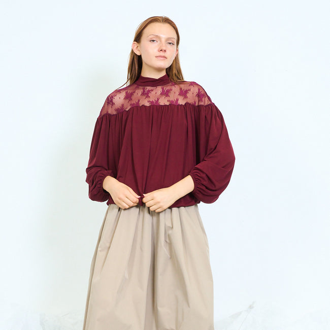 Bordeaux blouse with plain high collar, sheer floral lace yoke, gathered body, opaque voluminous long sleeves and gathered cuffs and hem; beige long skirt and shoes styled separately