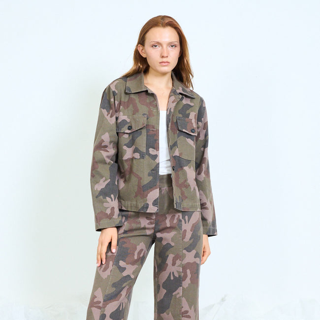Olive green and brown camouflage utility jacket with pointed collar, front buttons, buttoned chest flap pockets, lower front flap details and long sleeves; plain top, coordinating camouflage trousers and shoes styled separately