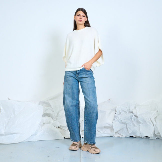 Model wearing a cream loose knit top with draped short sleeves and jeans