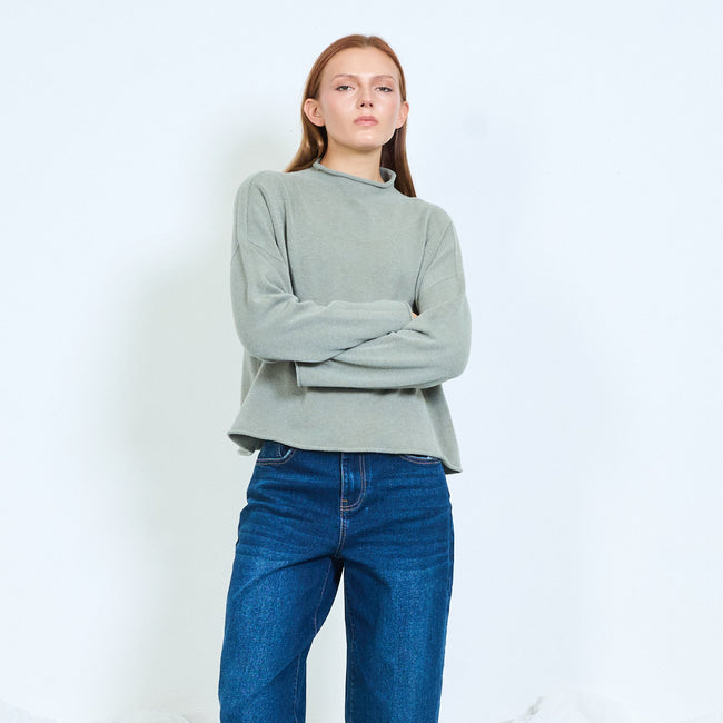 Sage green long-sleeve sweater with rolled neckline, shown with arms folded.