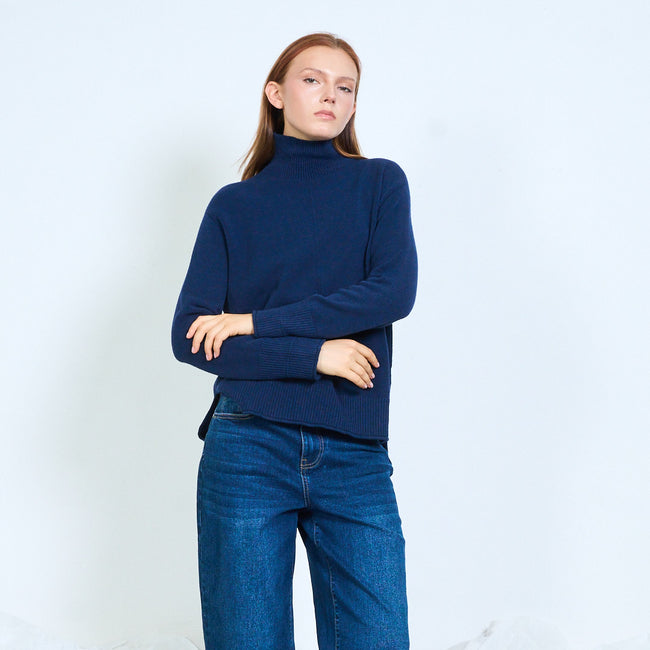 Navy blue high-neck sweater shown with arms crossed at the waist.