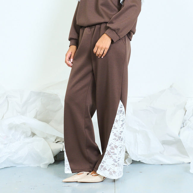 Side view of brown trousers with white floral lace inserts at the hems.