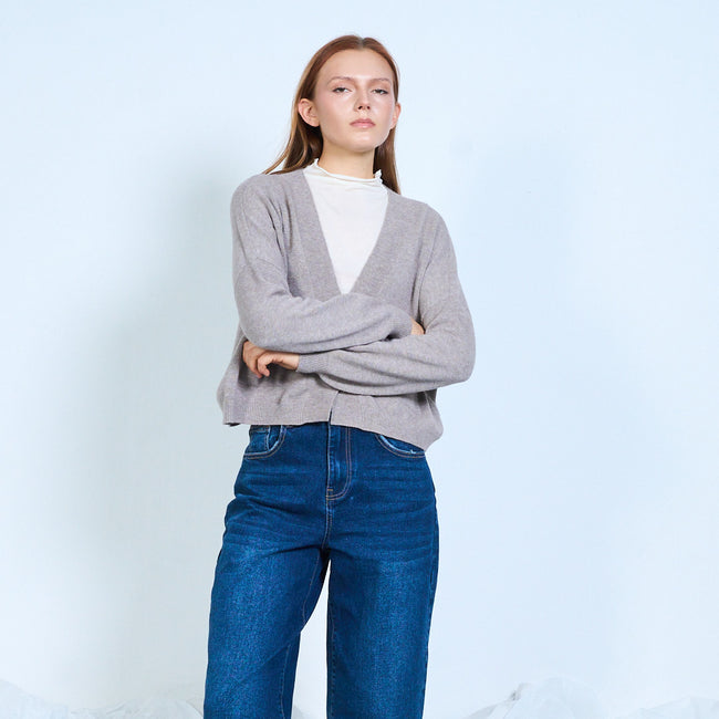Taupe V-neck cardigan worn over a white top, with arms folded.