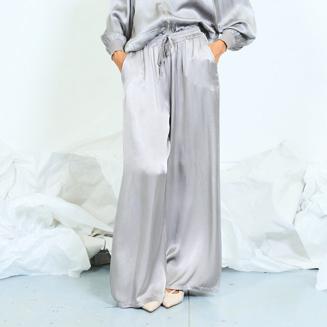 Silver-gray glossy wide-leg trousers with drawstring waist.