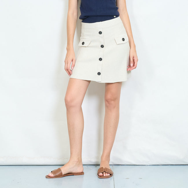 Front view of a light beige A-line mini skirt with dark buttons and flap pockets.