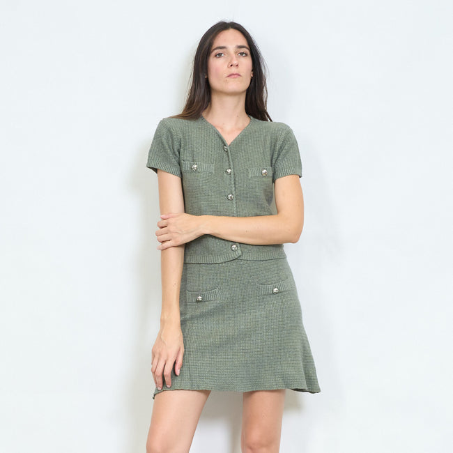 Model wearing an olive green short-sleeve button-front knit top and matching mini skirt.