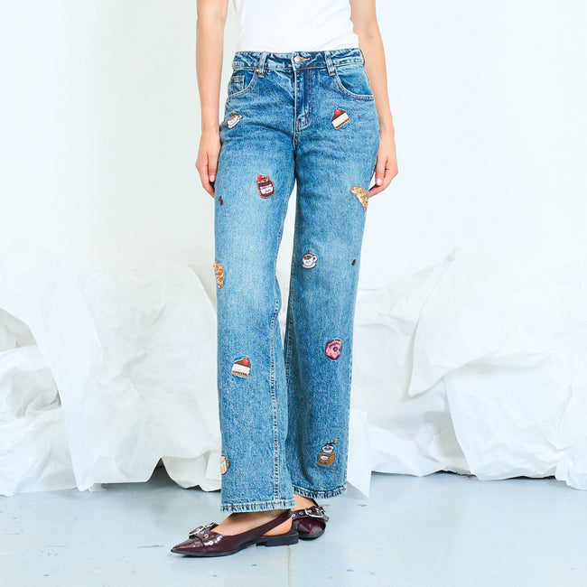 Front view of blue wide-leg jeans decorated with small food and drink motifs.