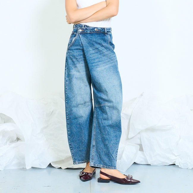 Front view of blue barrel-leg jeans with an asymmetric overlapping waistband.