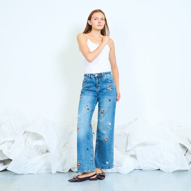 Model wearing blue wide-leg jeans decorated with small dog motifs.