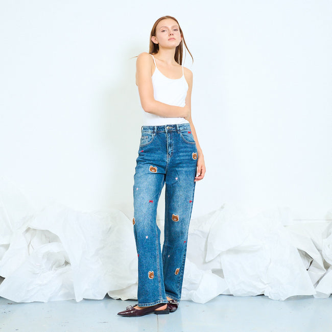 Model wearing blue jeans decorated with bear faces and small bows.