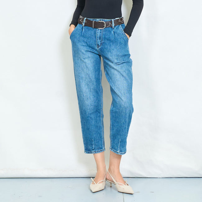Front view of blue cropped tapered jeans with front pleats and a dark belt.