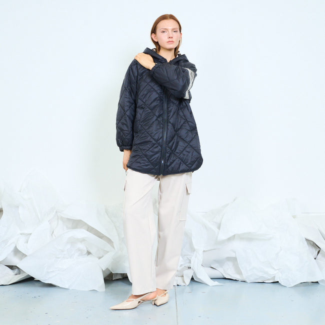 Full-length view of a model wearing a dark quilted hooded jacket with pale cargo pants.