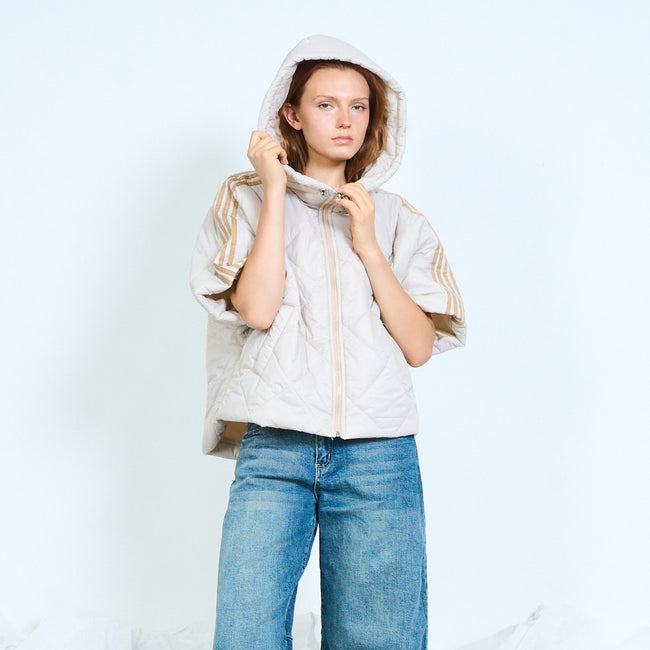 Model wearing a light greige hooded quilted jacket with short striped sleeves.