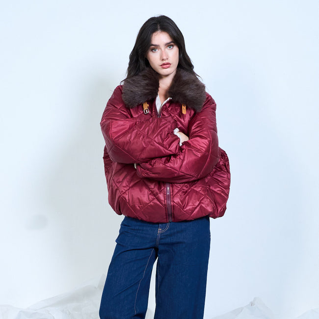 Model wearing a burgundy diamond-quilted jacket with a dark fluffy collar, arms crossed.