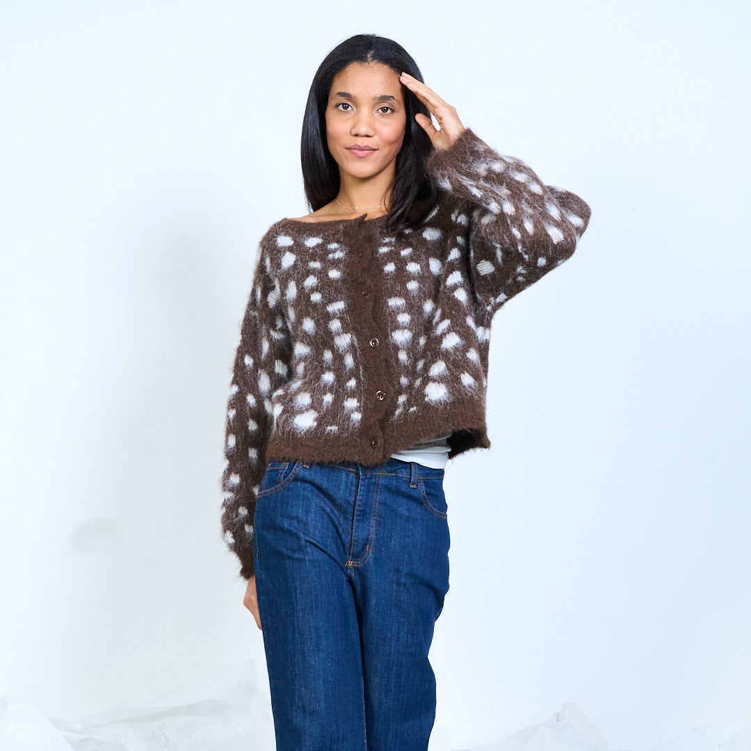 Model wearing a brown cardigan with pale spots, round neckline and balloon sleeves, front view with one hand raised