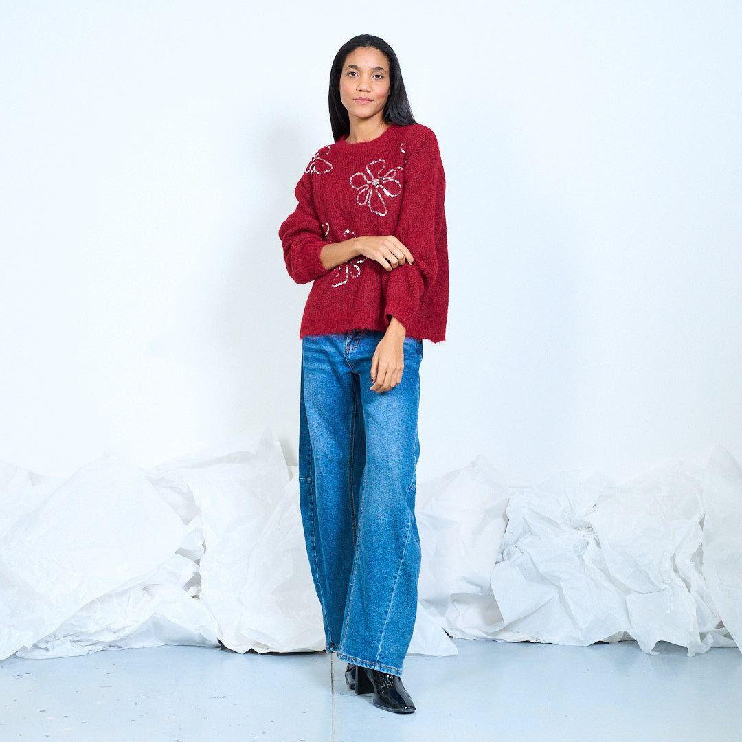 Model wearing a burgundy round-neck knit sweater with large shiny flower outlines, full-length front view
