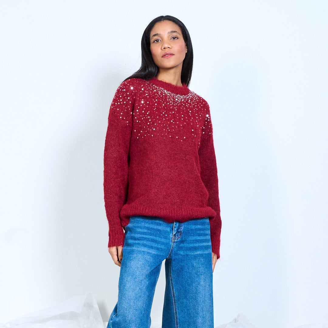 Model wearing a burgundy round-neck knit sweater with scattered shiny embellishments across the upper front, front view